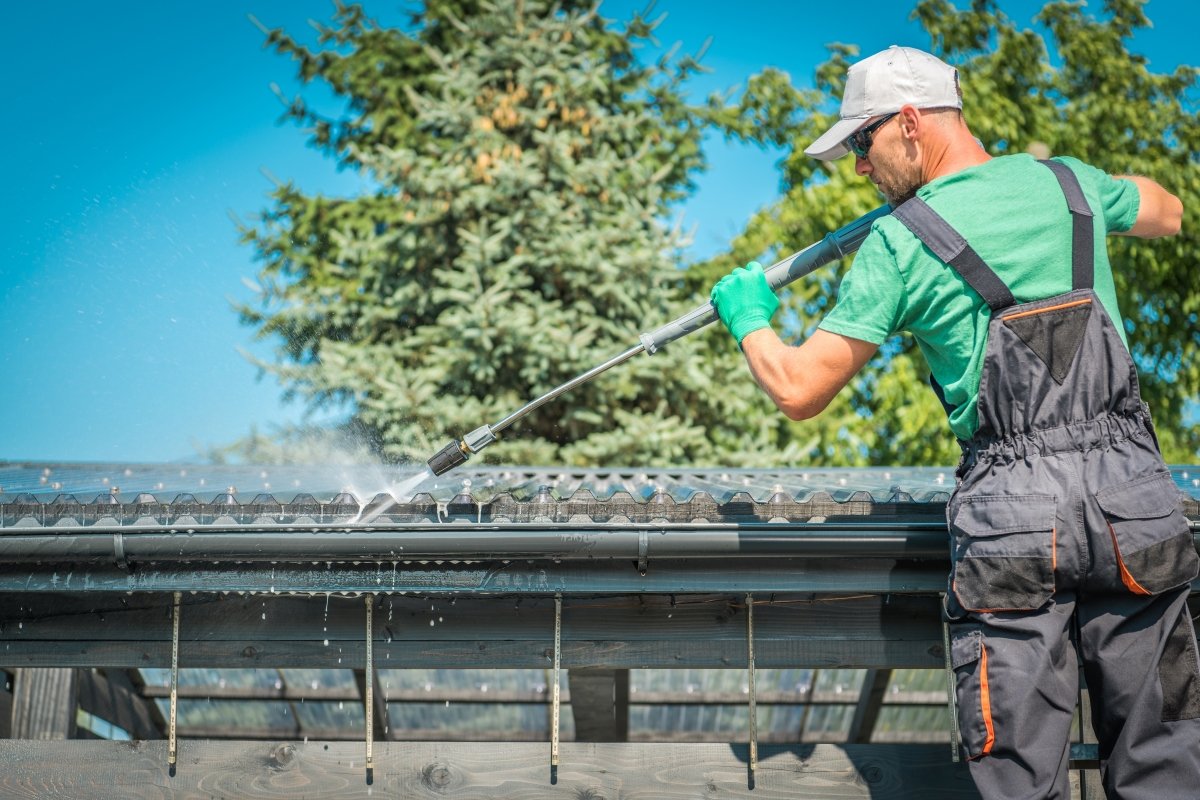 A man is on a latter and using water to clean his gutters.