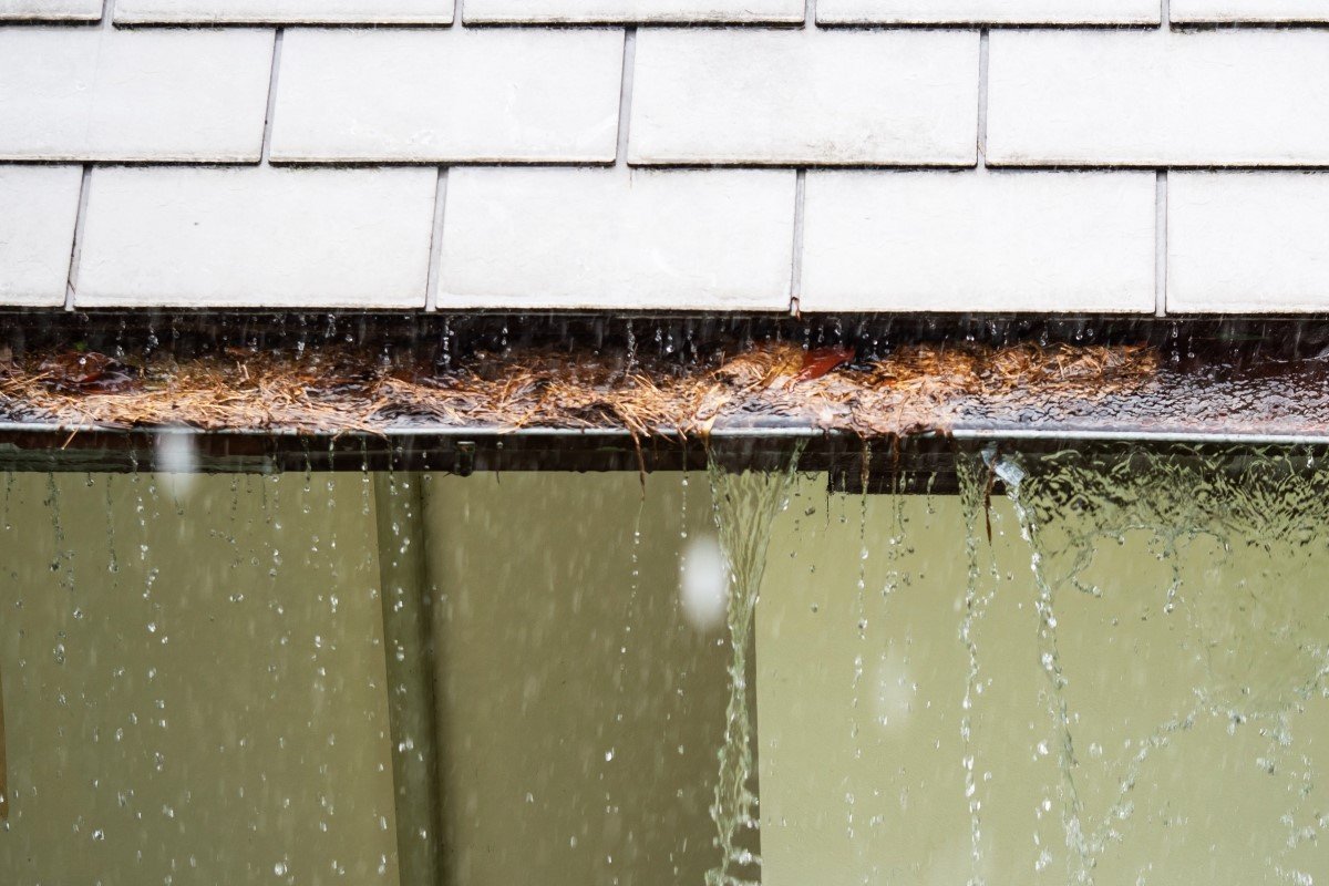 Close up on section of rain gutter clogged with leaves, debris on residential home during the rain.