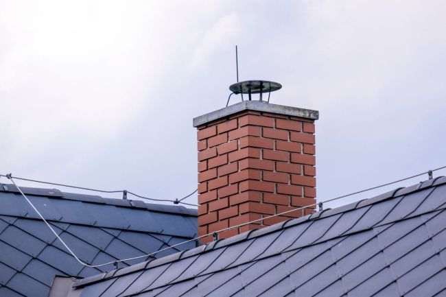 A red brick chimney is the focus in a photo of a roof.