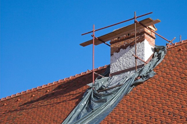 Scaffolding lines a brick chimney perched on a red tile roof.