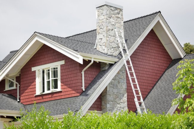 a silver ladder is propped up against the stone chimney of a red house.