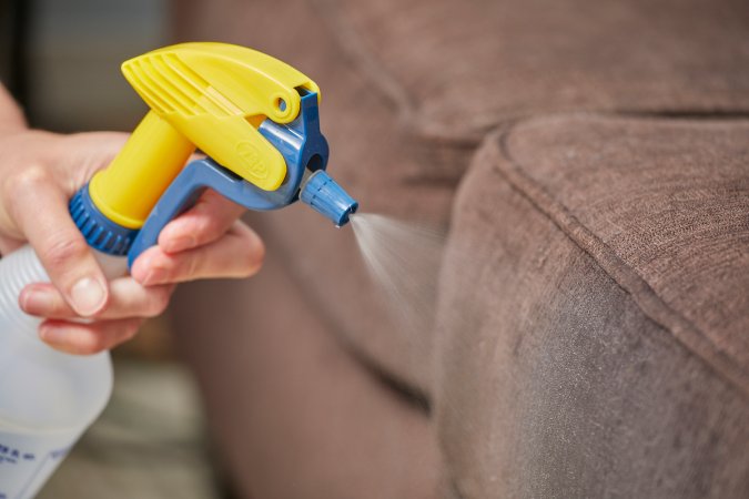 Woman sprays a brown couch with cleaning solution.