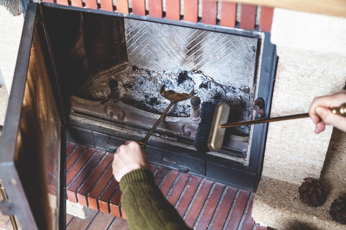 Man cleans ashes from the fireplace with fireplace tools.