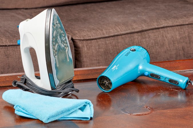 A hairdryer, clothes iron, and microfiber cloth on a wood table.