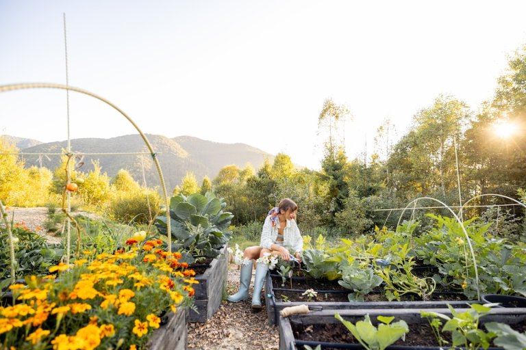 A woman in rain boots works in her garden, which has been constructed using permaculture.