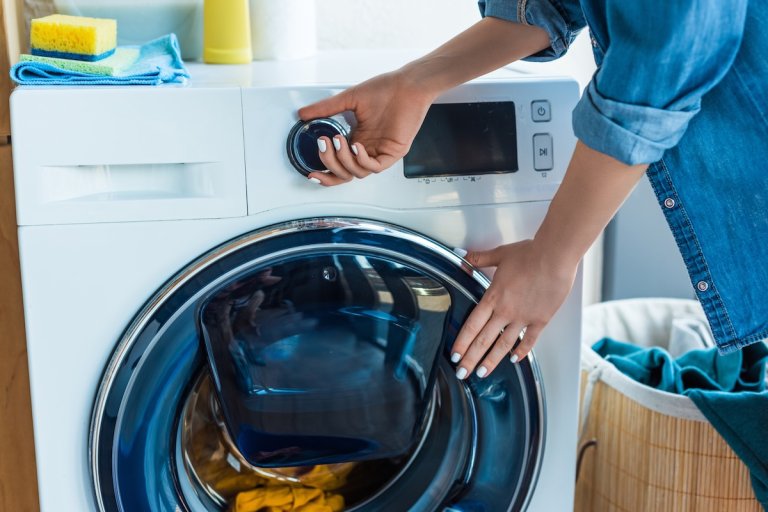 A women in a denim blouse changes the settings on her modern washing machine.