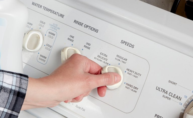 Woman turns the settings dial on a white washing machine's control panel.