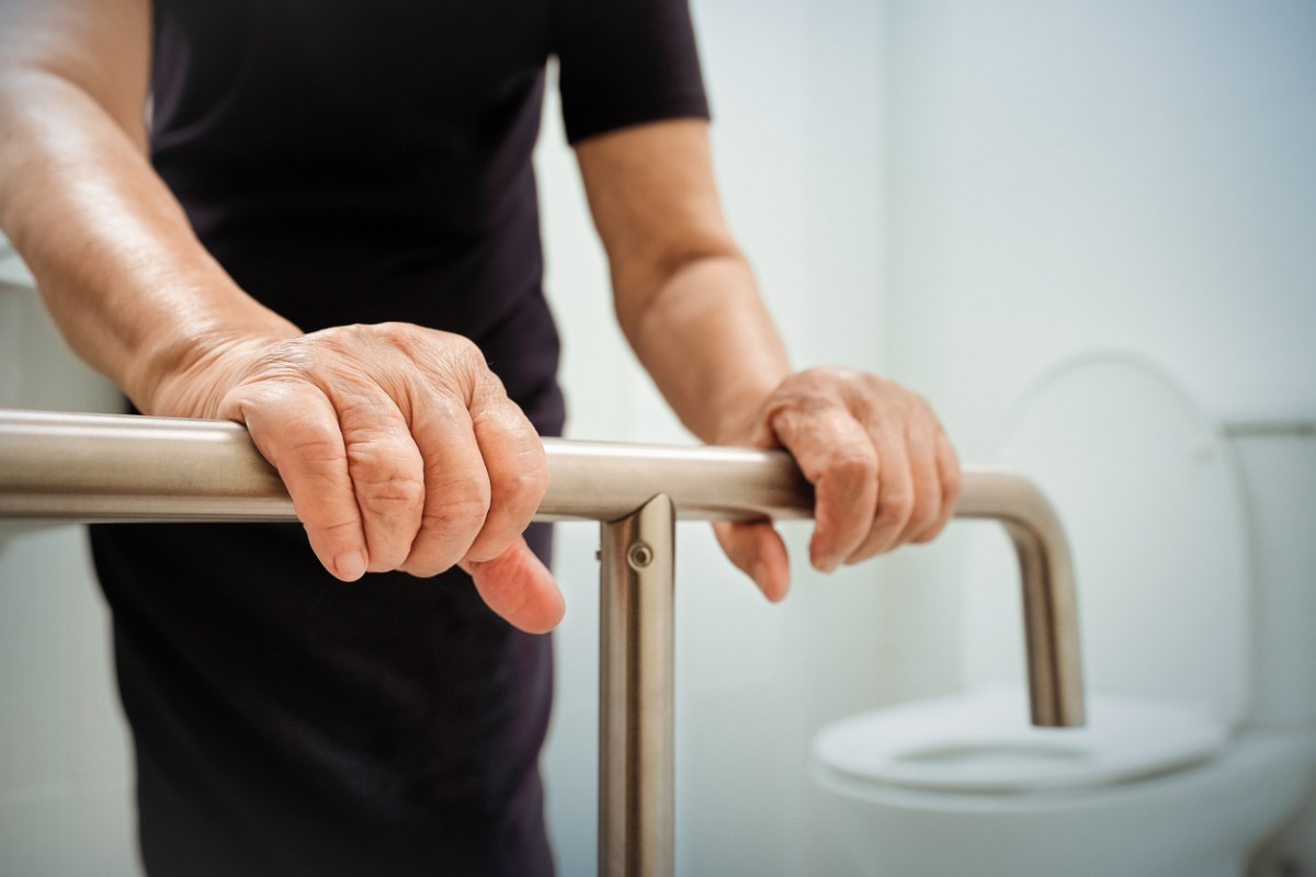 A close up of a person holding onto grab bars in a bathroom.