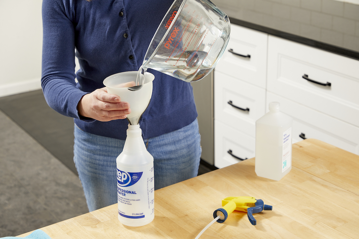 Woman pouring alcohol from a measuring cup into a spray bottle.