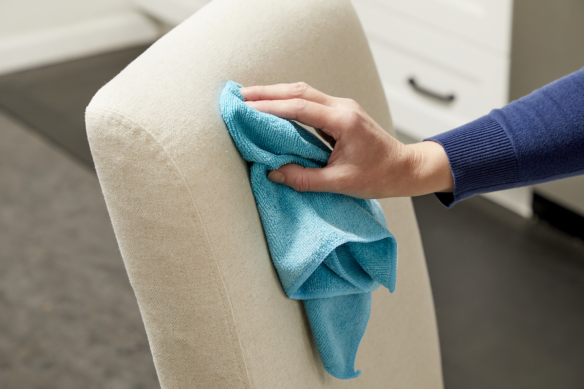 Woman daubing upholstered chair with a blue microfiber cloth.
