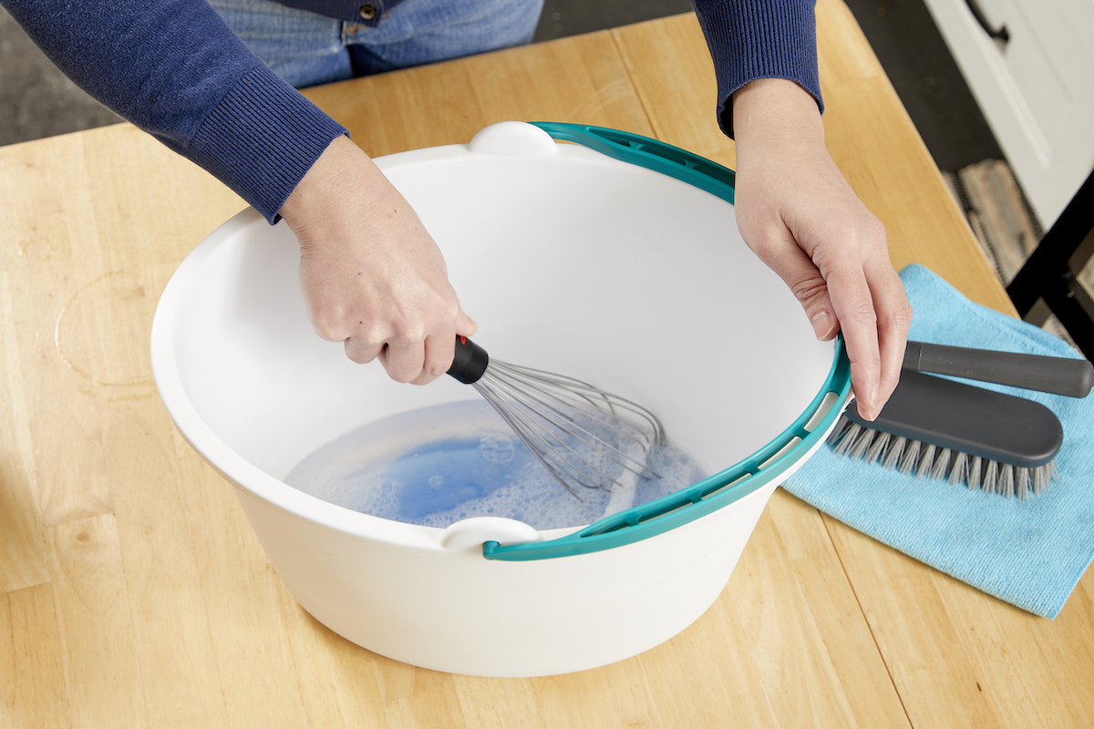 Woman whisking liquid upholstery cleaner in a bucket.