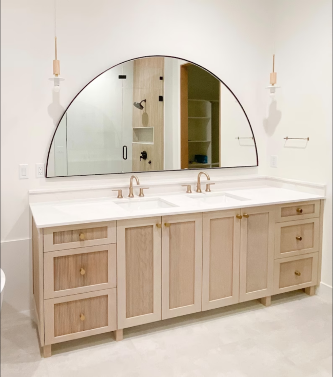 Wide half-moon bathroom mirror hanging over a double vanity sink