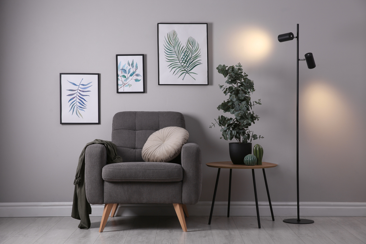 Potted indoor eucalyptus plant sitting on a side table beside a gray chair and black lamp