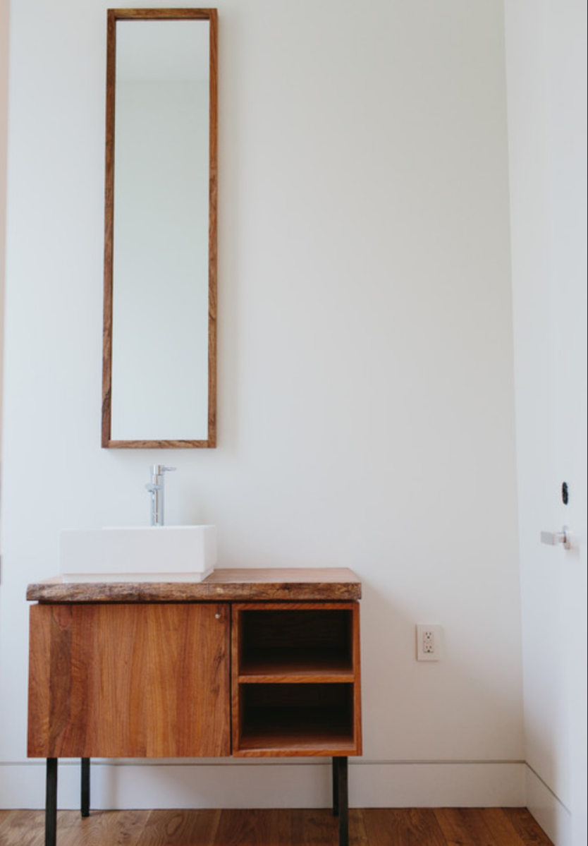 Long and narrow mirror over a simple wood bathroom vanity.