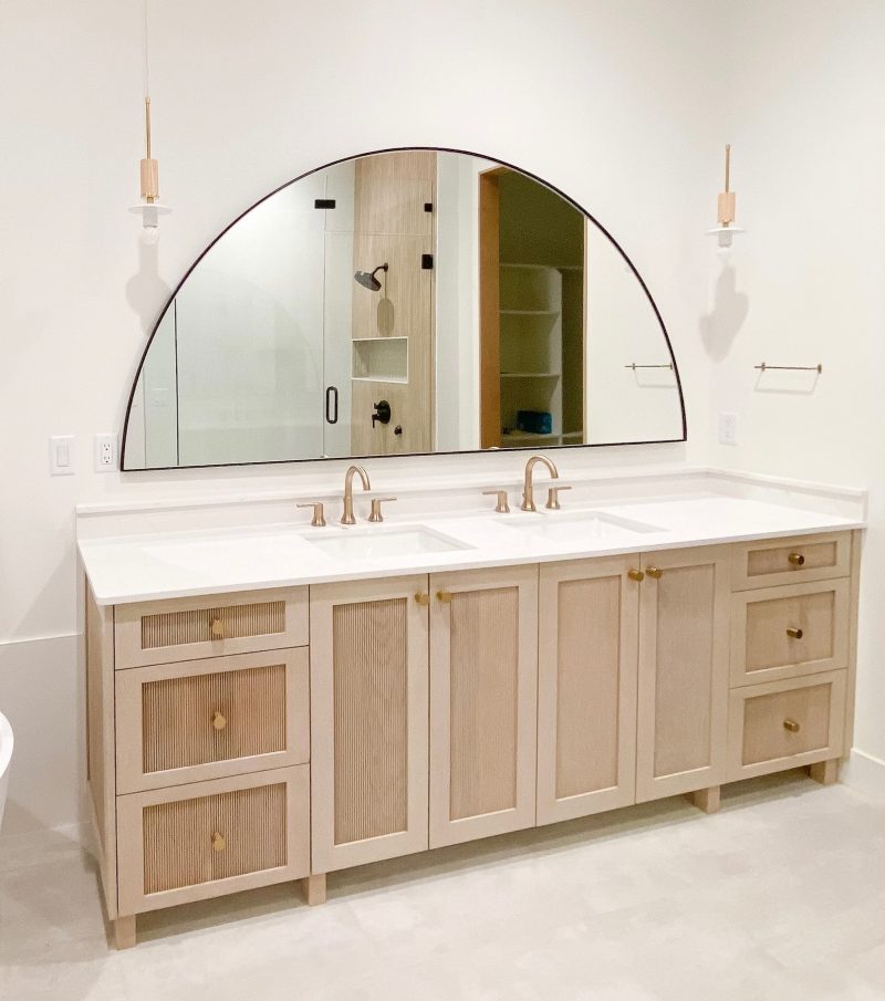Half moon-shaped bathroom mirror over a wood vanity.