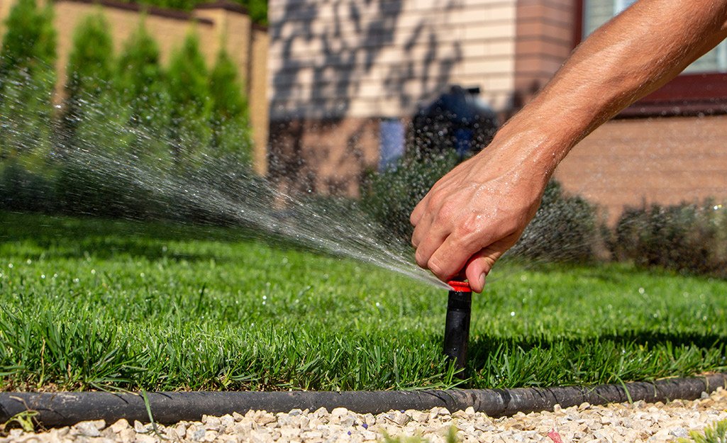 Person adjusting or fixing a sprinkler head on green grass.