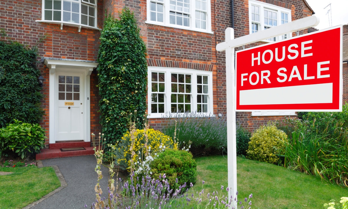 A brick home with a red for sale sign. 
