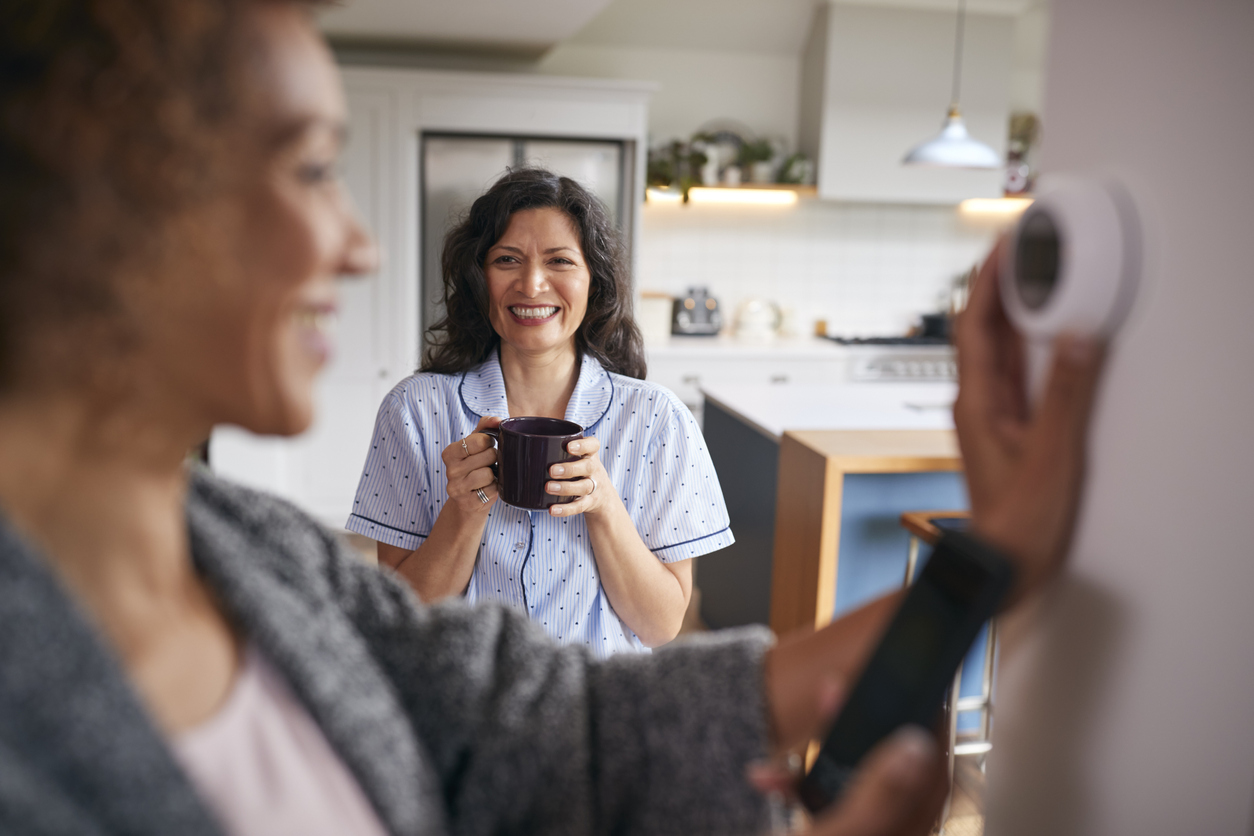Woman adjusting a smart thermostat, with another woman in background.
