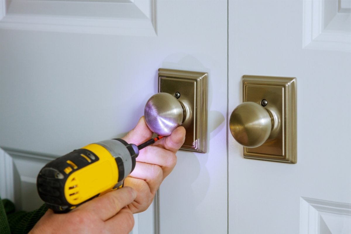 Person uses an electric screwdriver on an indoor doorknob set.