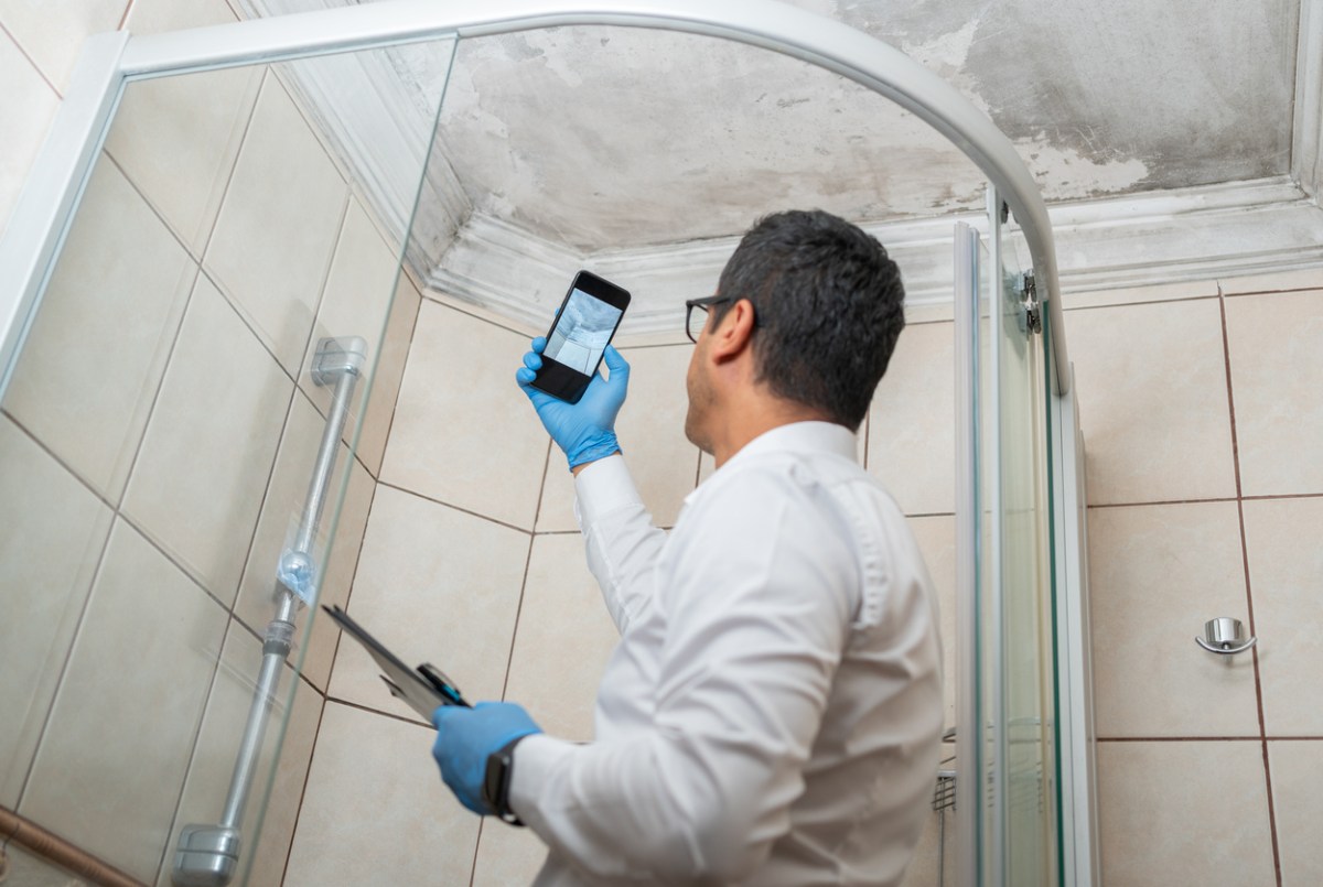 An inspector uses a phone to photograph mold in a shower.