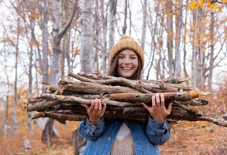 Young woman wearing a wool cap and heavy jacket collects long branches for firewood.