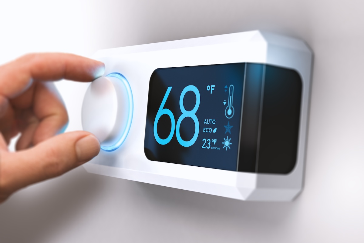 Hand turning a home thermostat knob to set temperature.