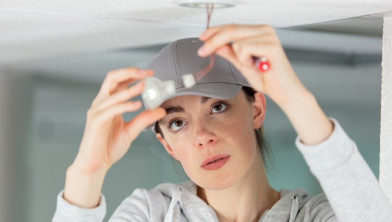 Closeup of a woman changing an overlead light bulb in her home.