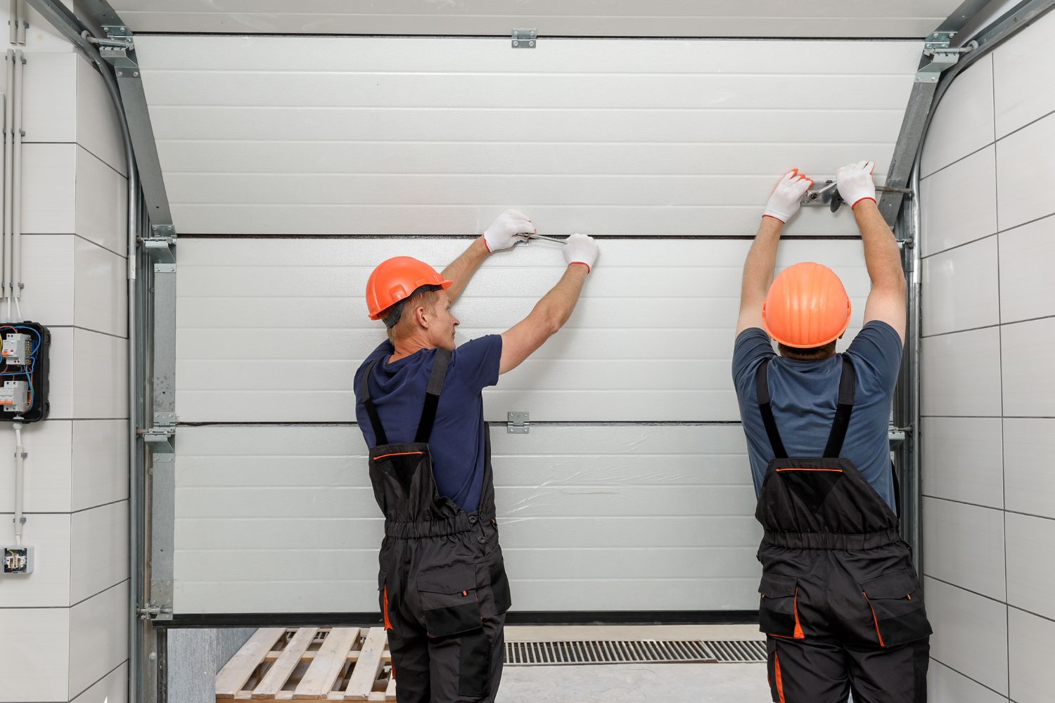 Two workers in orange hard hats install a garage door.