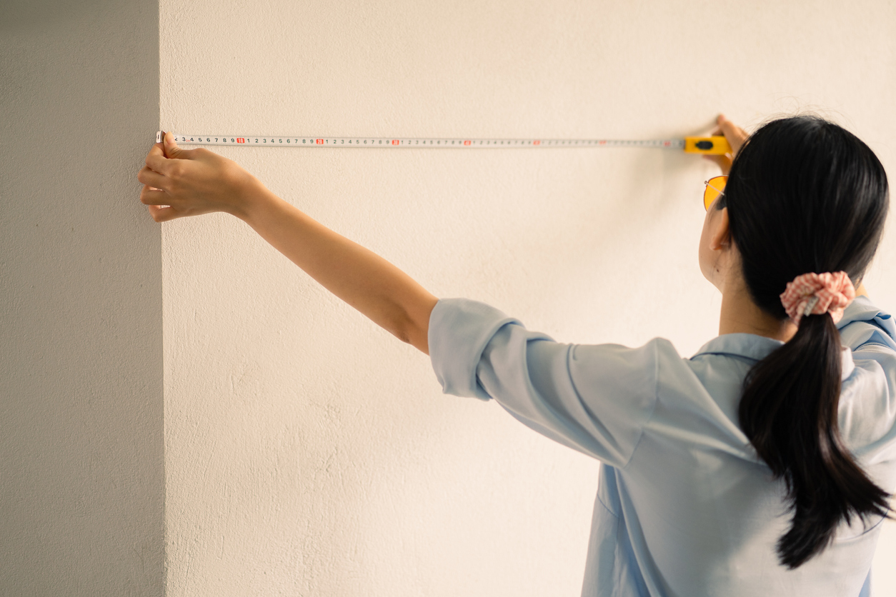 Person measuring a white wall with a tape measure