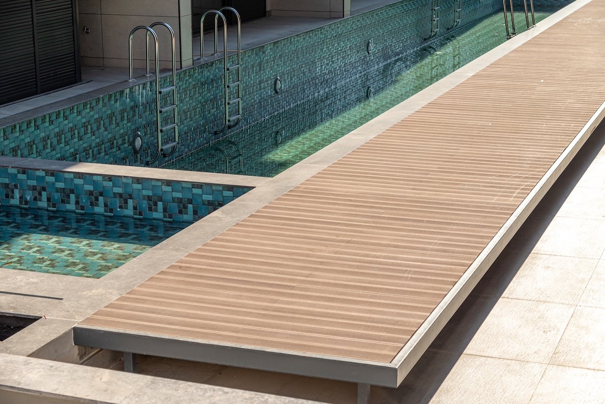 A path made of composite decking runs along a pool's edge.