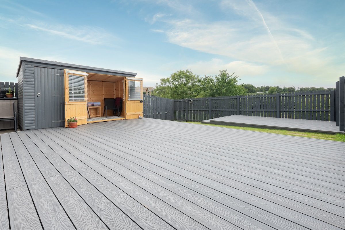 A modern patio area built with a slate grey composite decking material, with a small shed nearby.