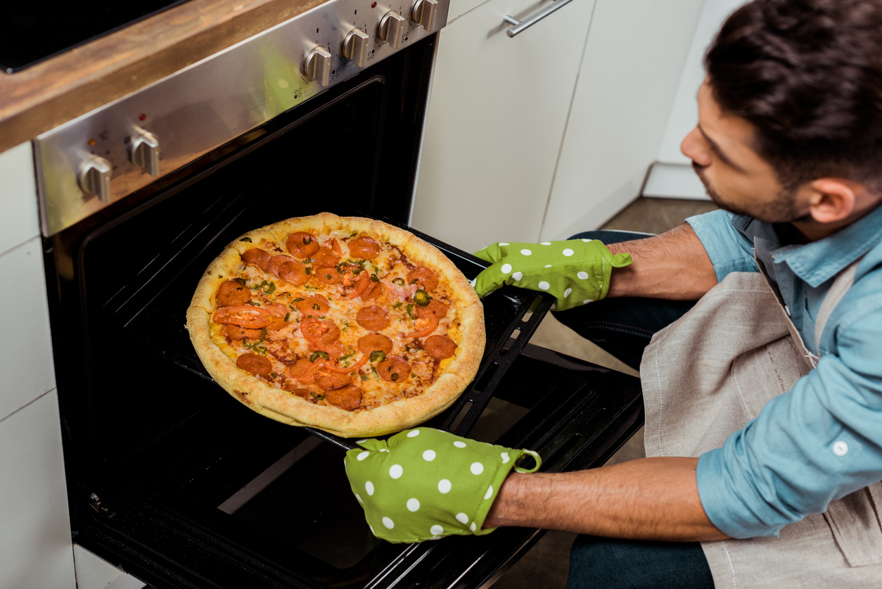 iStock-1070231674 work gloves man taking pizza out of oven with oven mitts