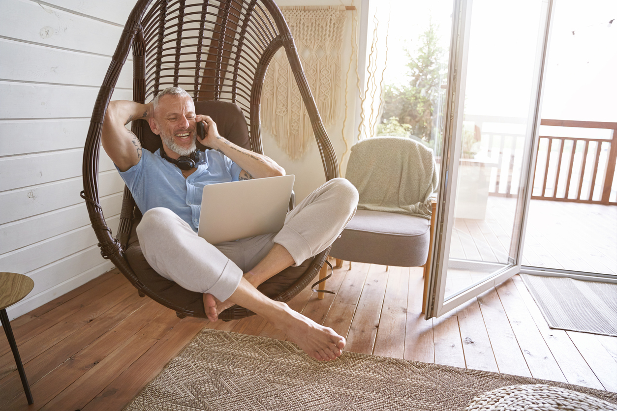 Middle-aged man sitting in a hanging chair in a living room, talking on the phone.