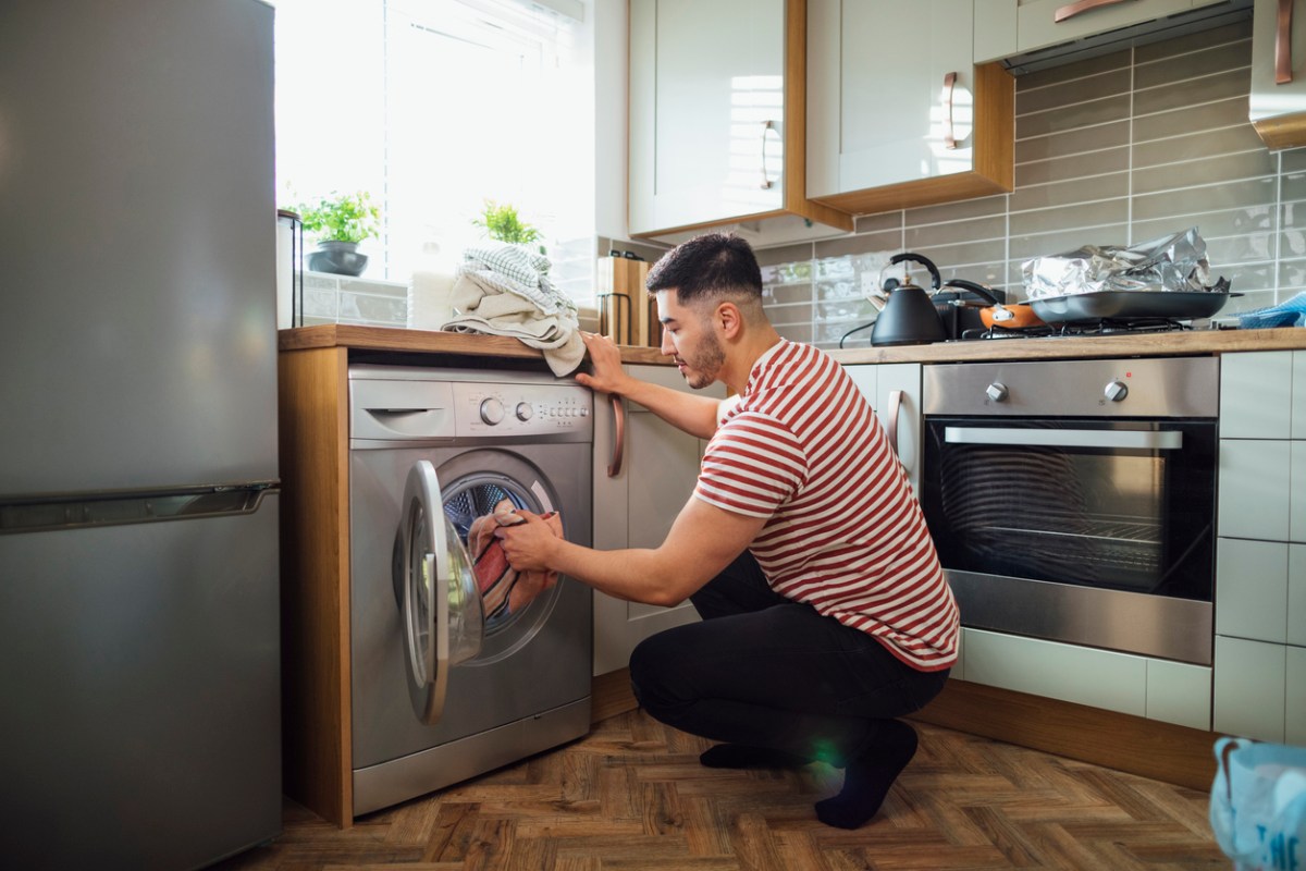 iStock-1290513514 appliance maintenance man doing laundry in kitchen