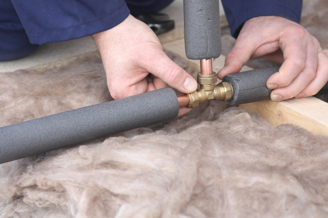Person installs foam insulation over copper pipes.