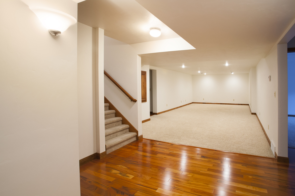 A well-lit finished basement with shiny wood floors and beige paint on the walls.
