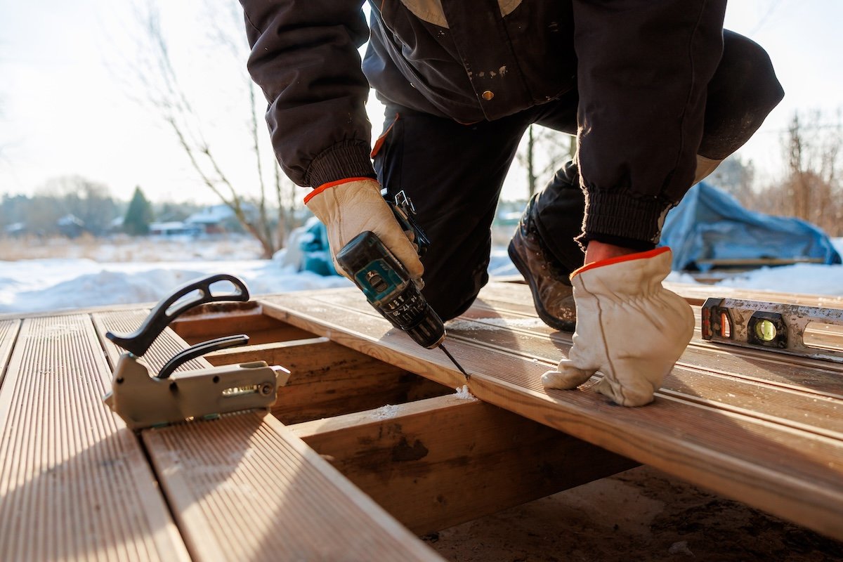 A carpenter uses a drill to install composite decking.