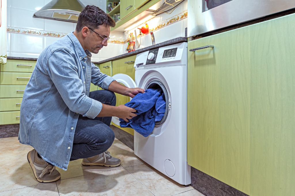 istock - 1367022943 -laundry room decor pantry organization man putting clothes in dryer