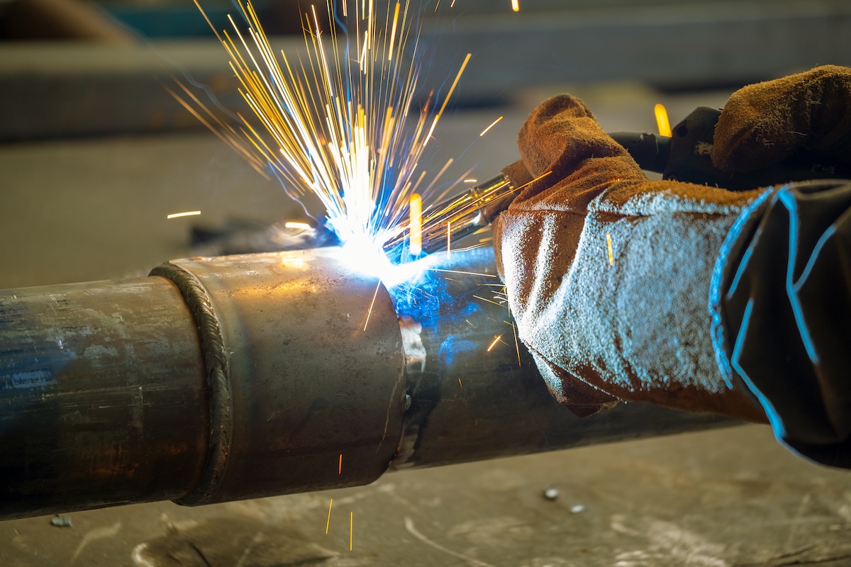 A welder MIG welding a large, steel pipe. 