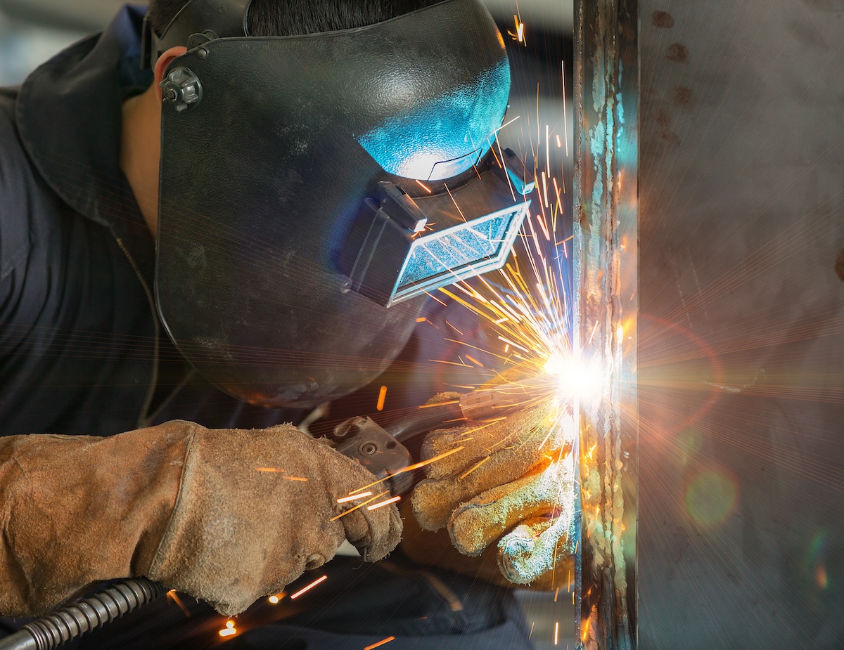 A professional MIG welder wearing protective headgear and gloves  as he works. 