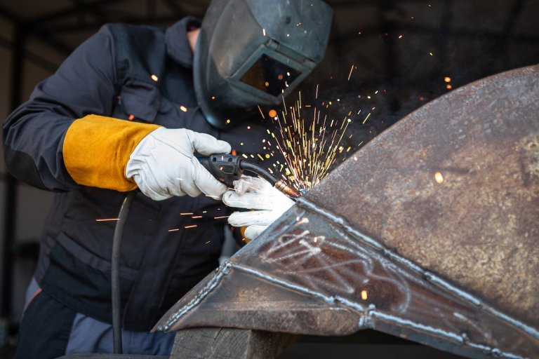A welder in protective gear works on a large piece of sheet metal.