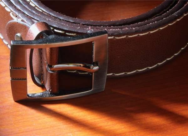 Brown leather belt rolled up on a wood table.