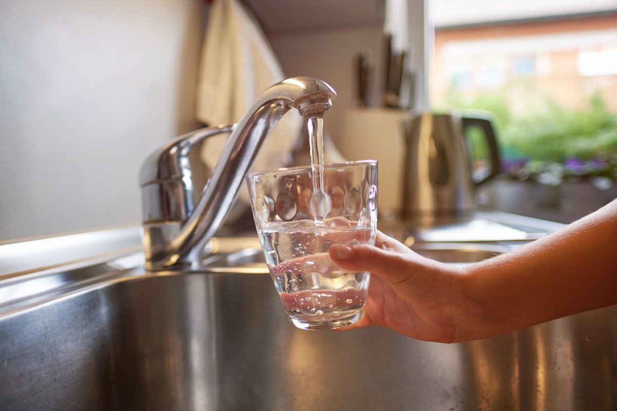 Small hand holds a glass under a kitchen tap to catch water.