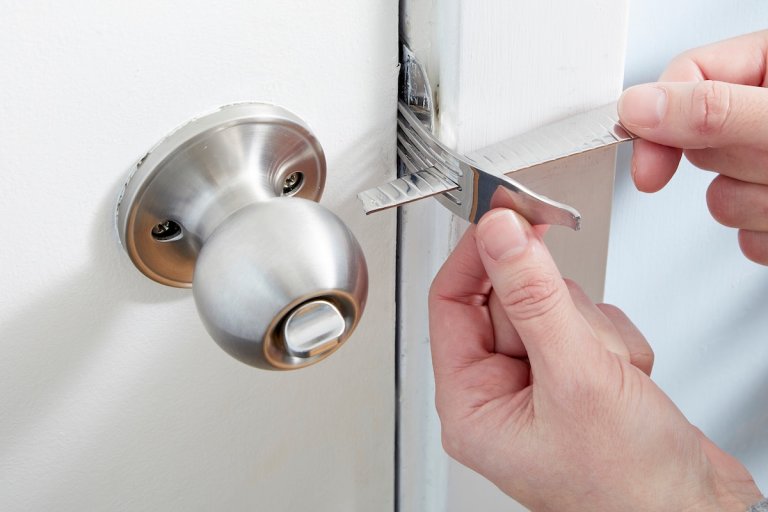 Person puts tines of a broken fork into a door near the strike plate, inserting the handle of the broken fork through some of the tines.
