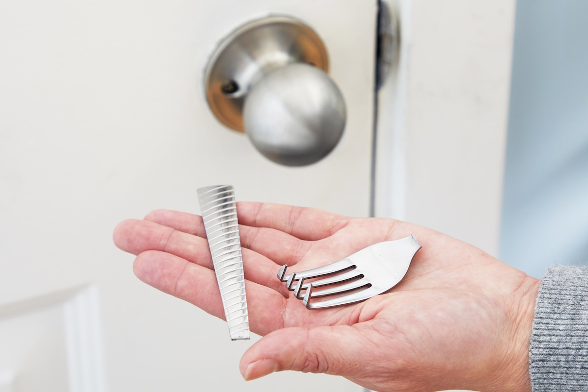 Woman holds two pieces of a broken fork in the palm of her hand, in front of a closed door.