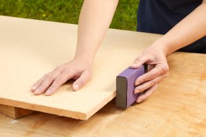 Woman uses a sanding block to sand the edges of particle board.