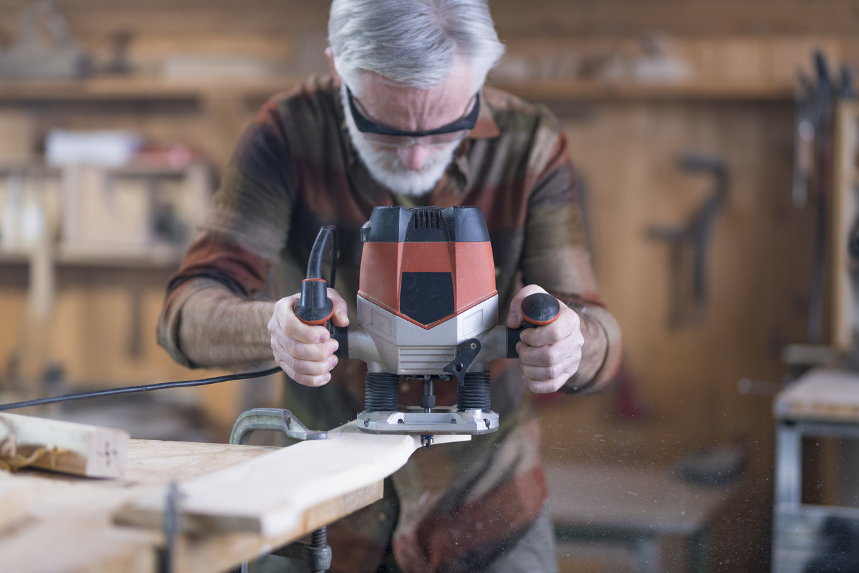 Man wearing safety glasses uses a router in a workshop.
