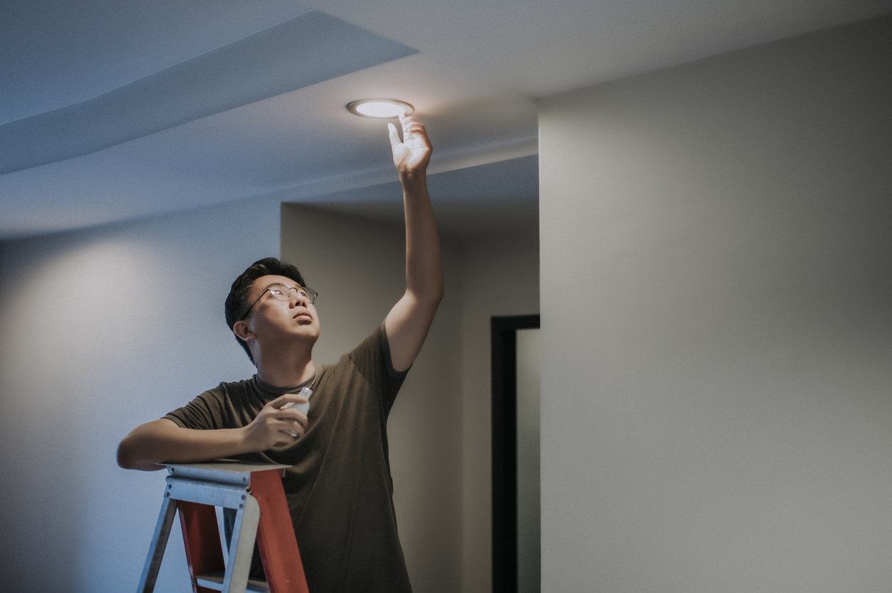 Man on ladder changes to LED bulb in ceiling light.