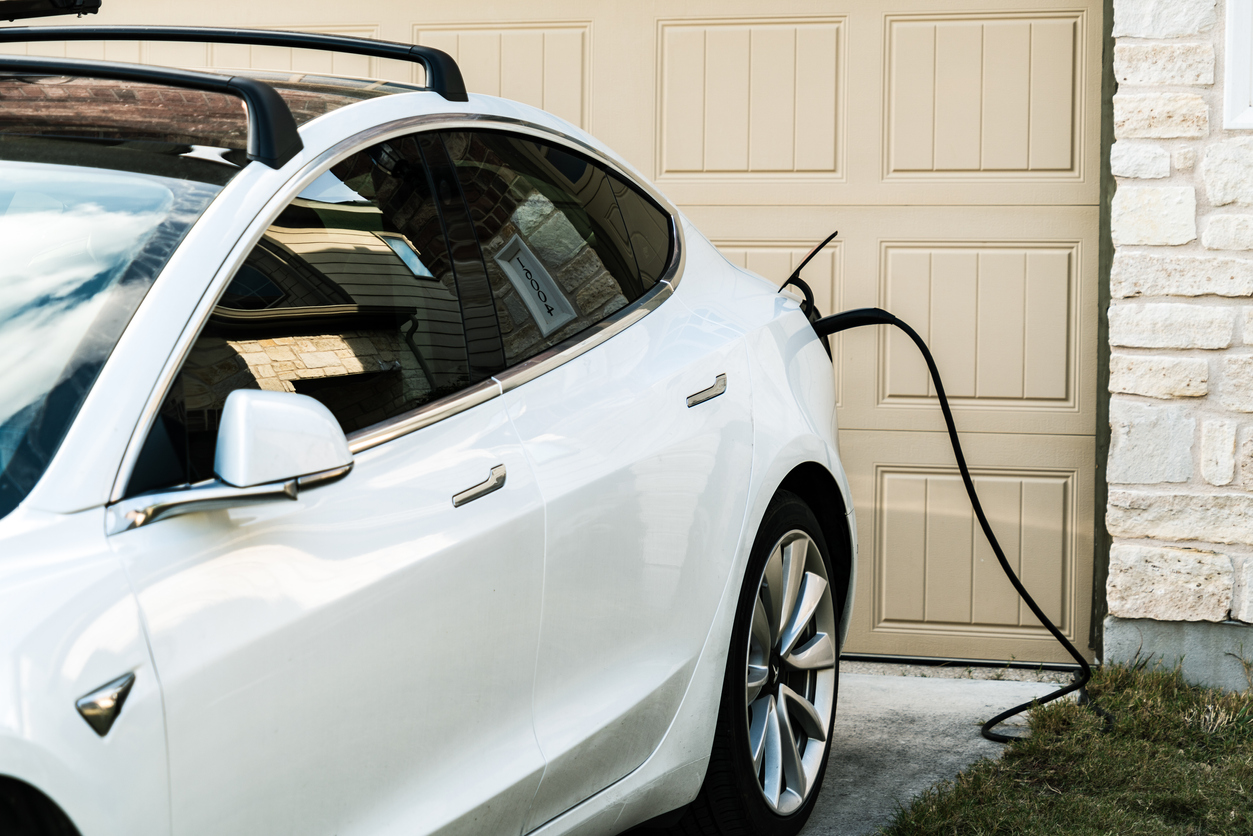 White electric vehicle charges from outlet outside a home.