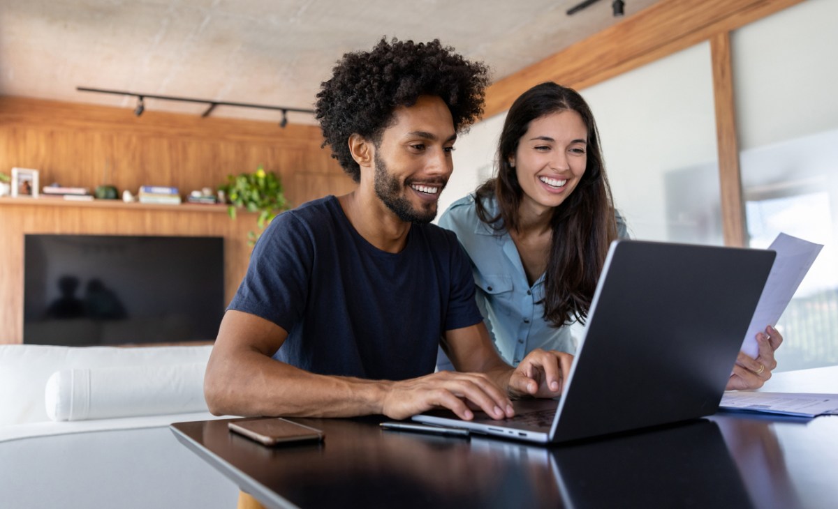 Smiling, young couple does laptop in modern home on laptop.